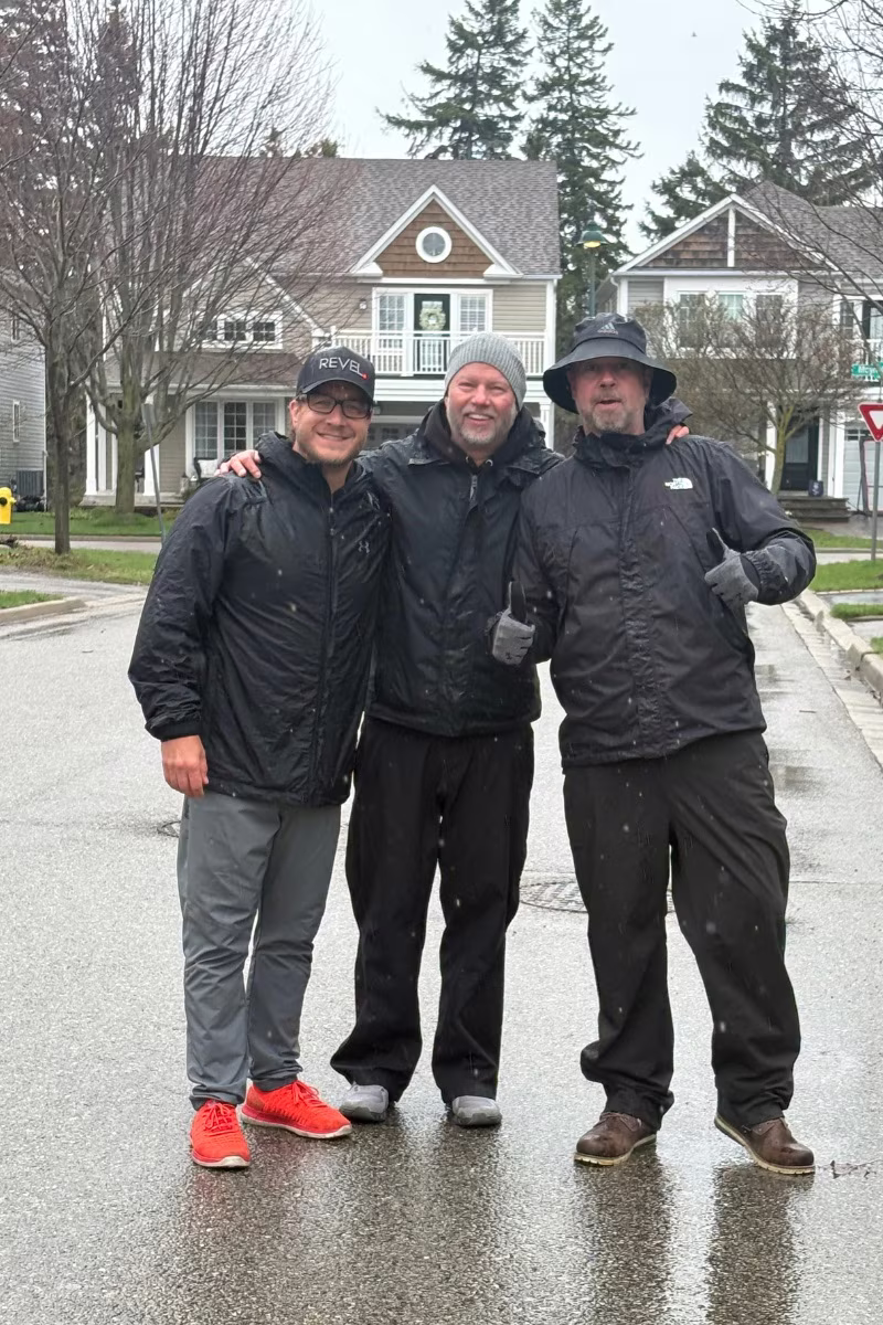 Doug Gordon, Rich Gordon and Dan Gregoire arm in arm on a Lakeside street in South Ajax, in front of the neighbourhood's signature homes on a rainy morning