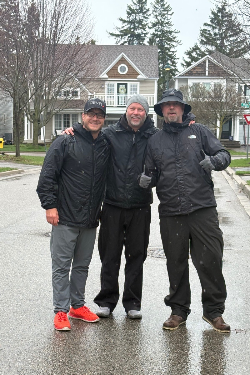 Doug Gordon, Rich Gordon and Dan Gregoire arm in arm on a Lakeside street in South Ajax, in front of the neighbourhood's signature homes on a rainy morning